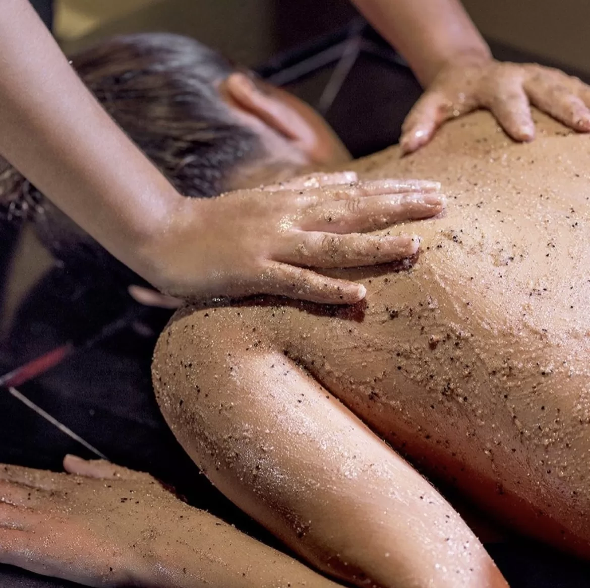 Close-up of hands applying exfoliating scrub to a guest's back during a hammam ritual