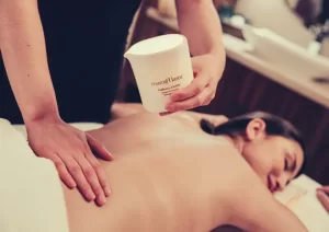 A therapist warming and pouring a marocMaroc Paillettes d'Ambre massage candle over a guest's back